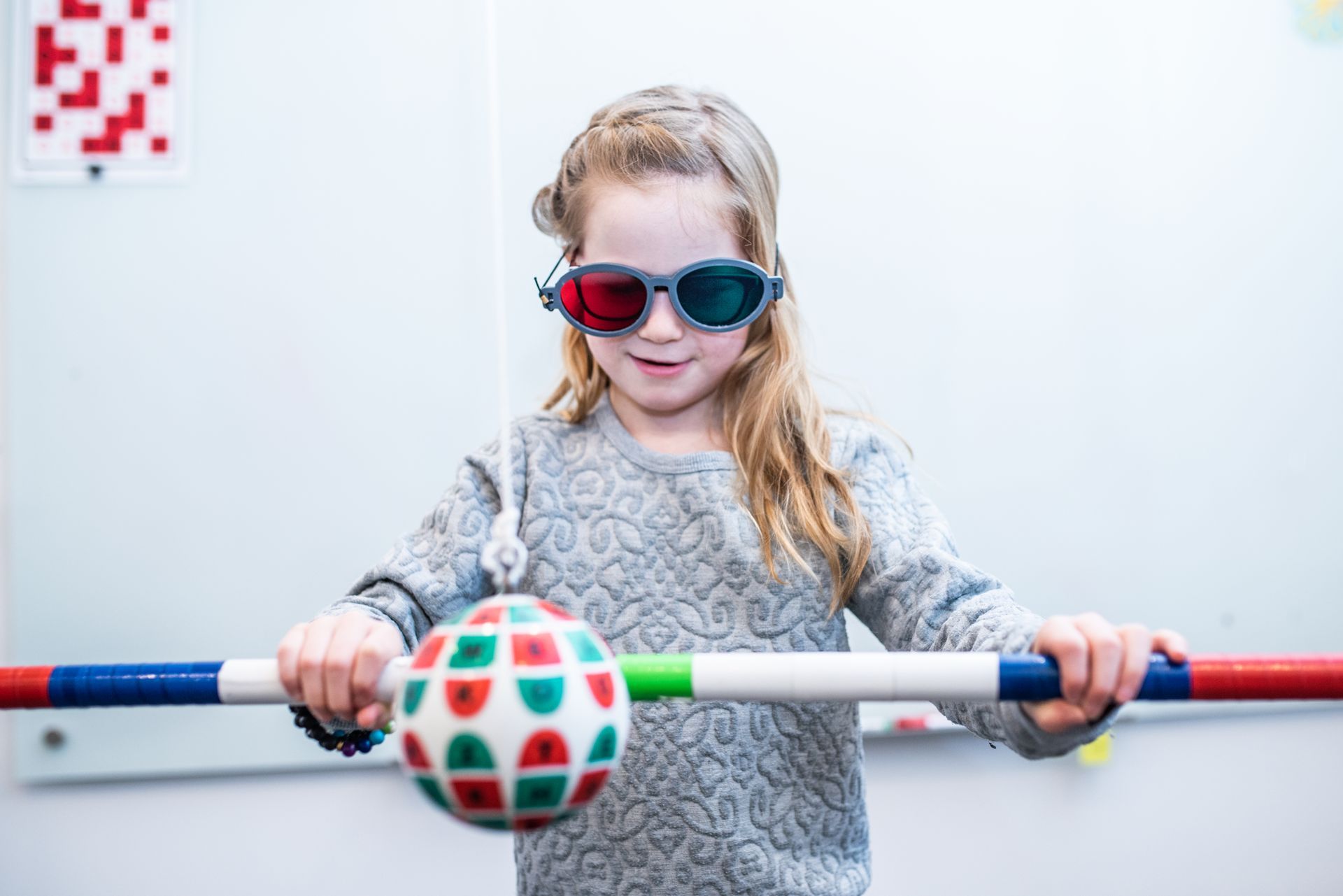 A little girl wearing 3d glasses is holding a ball and a stick.