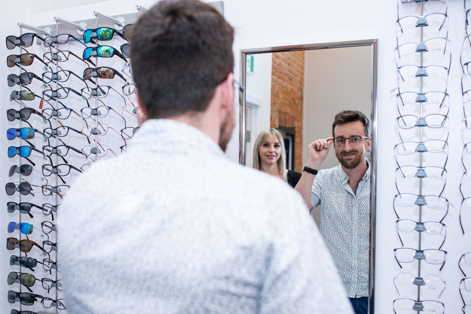 A man is trying on glasses in front of a mirror.