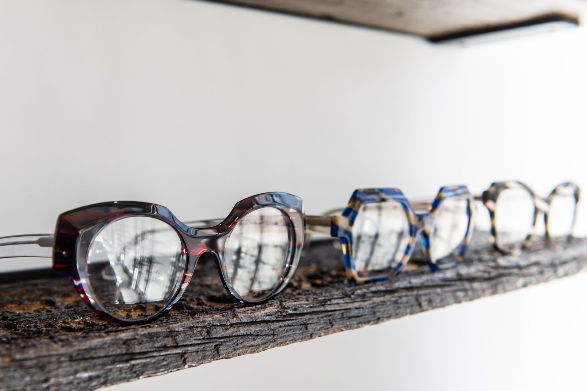 A row of glasses sitting on top of a wooden shelf.