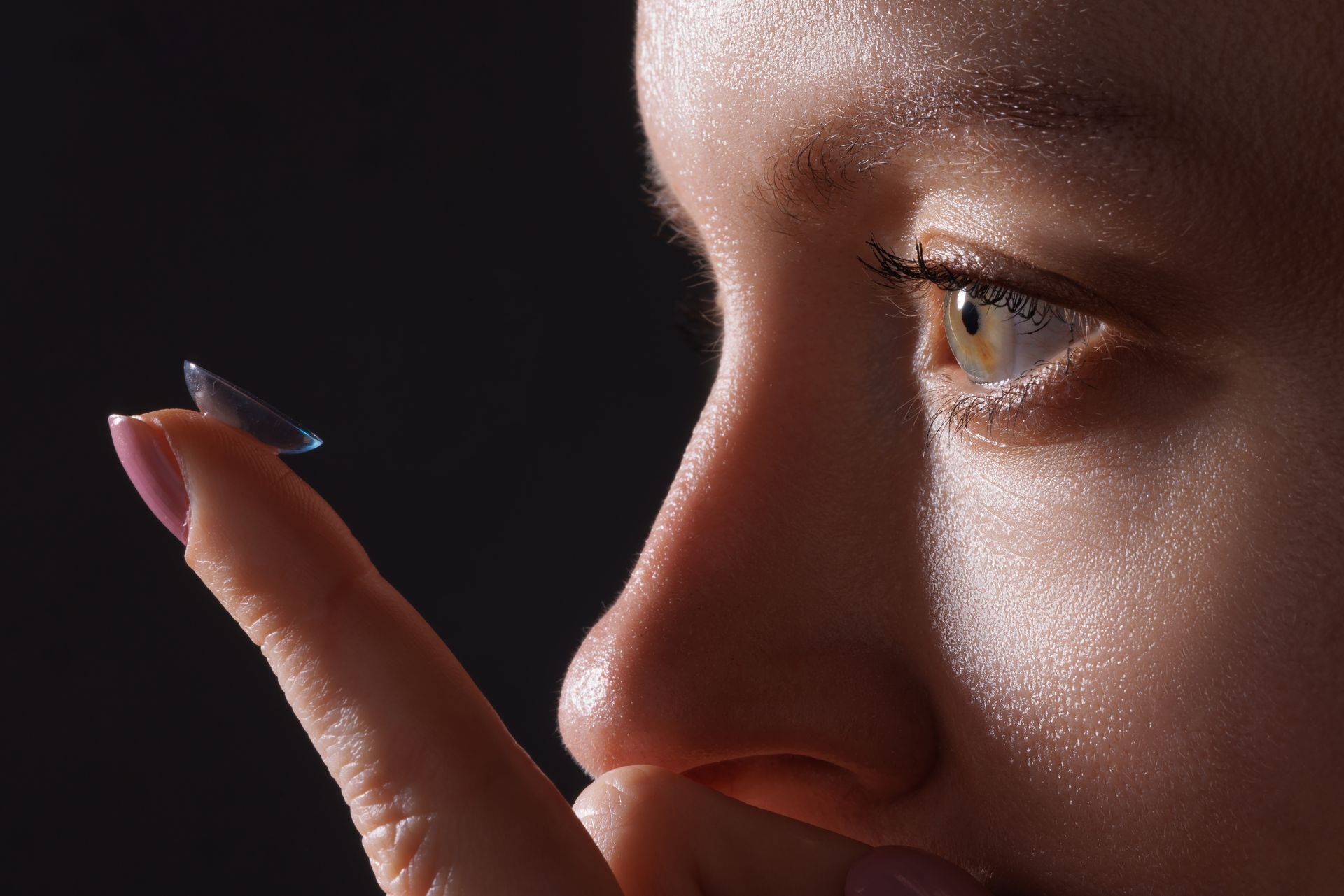 A woman is putting a contact lens on her finger.