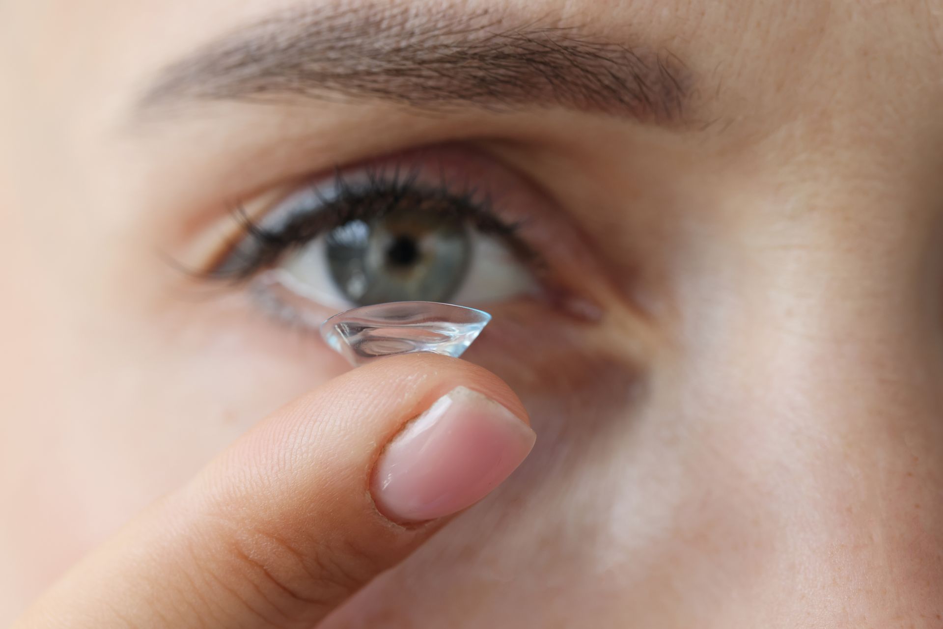 A woman is putting a contact lens in her eye.