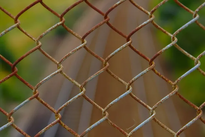 A close up of a rusty chain link fence with a blurry background.