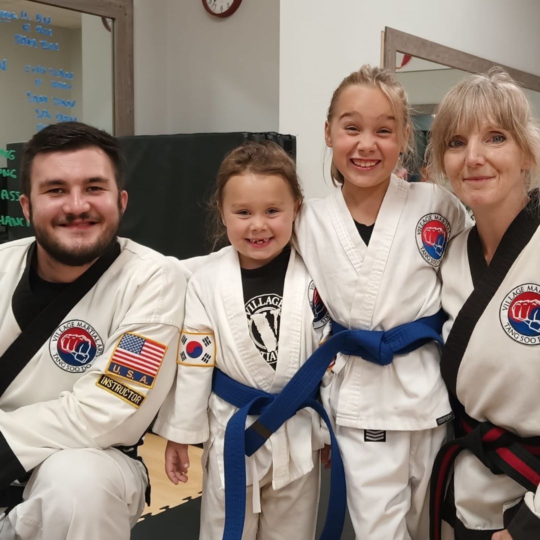 Two people grappling on a mat, one in a black gi, the other in a rash guard, legs entangled.