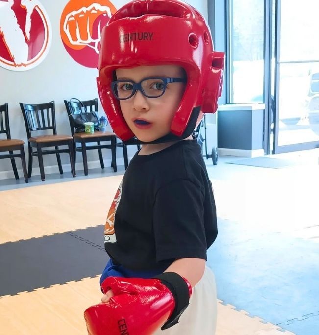 Family in Jiu-Jitsu gis poses. Indoors, blue mats, a smiling woman in the middle, around a seated man with a beard.