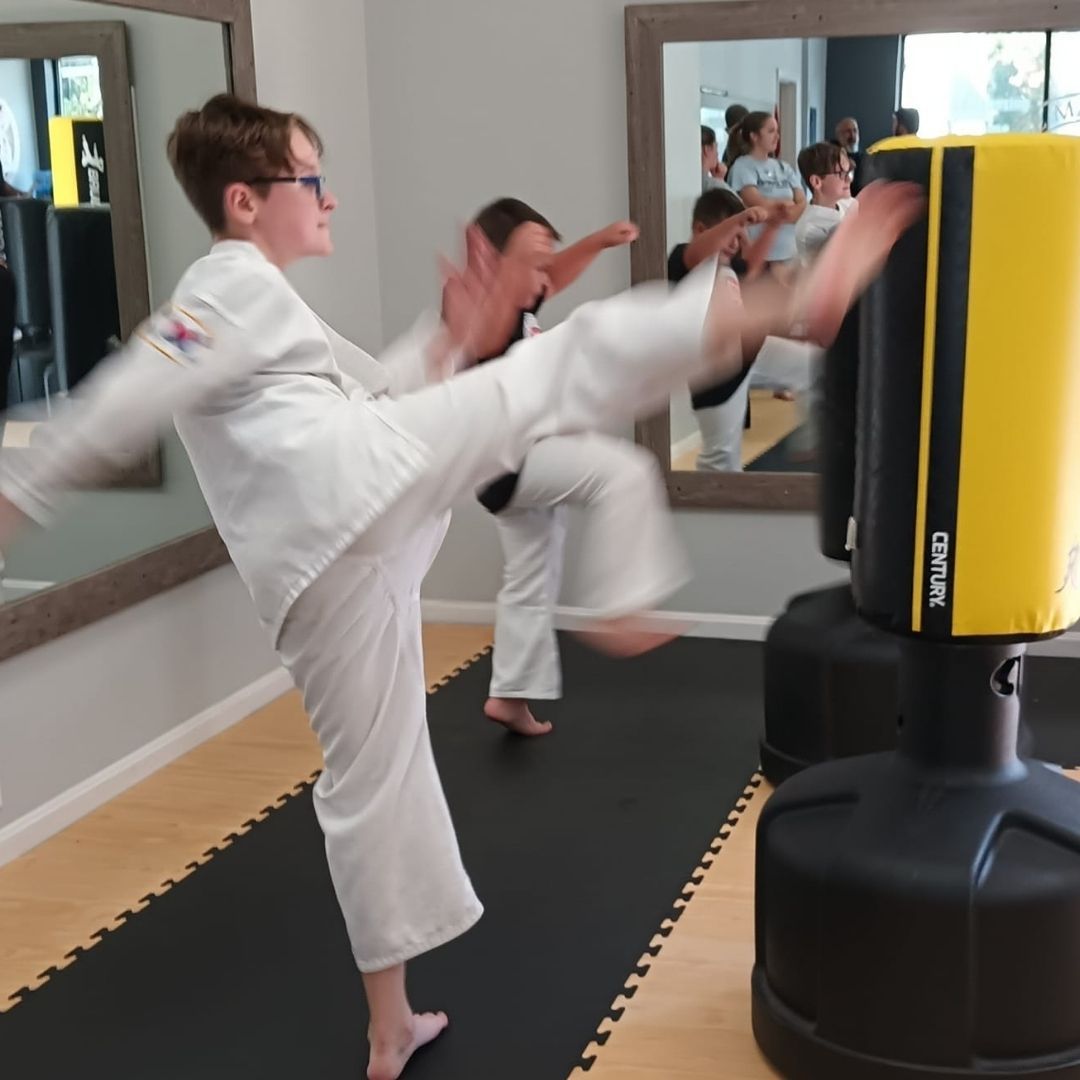 Two boys on a mat practicing Jiu-Jitsu. One boy is on top, giving a thumbs-up.