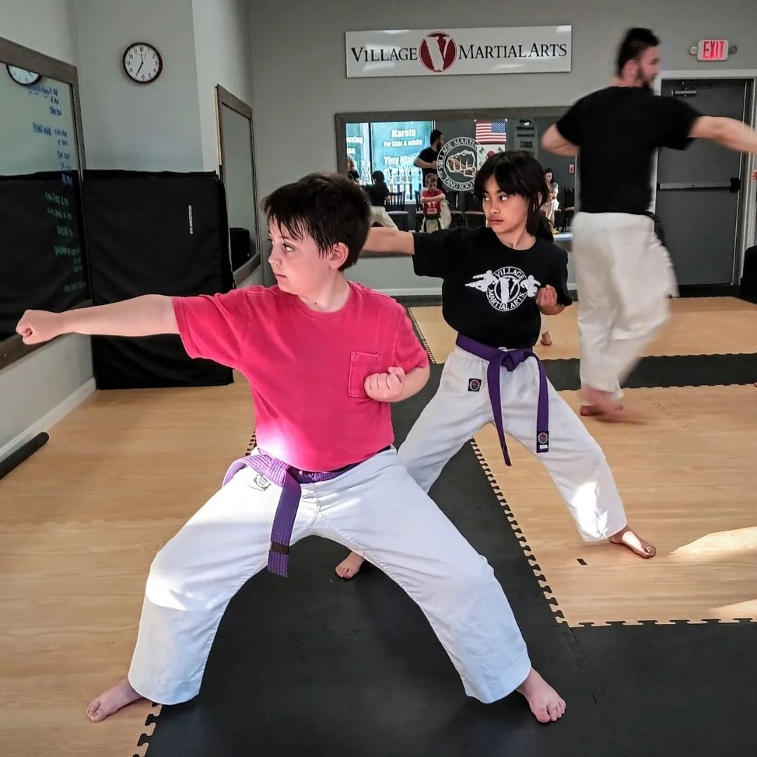 People practicing Brazilian Jiu-Jitsu. One person on the ground, another on top; two others grappling nearby. Black gis, indoor setting.