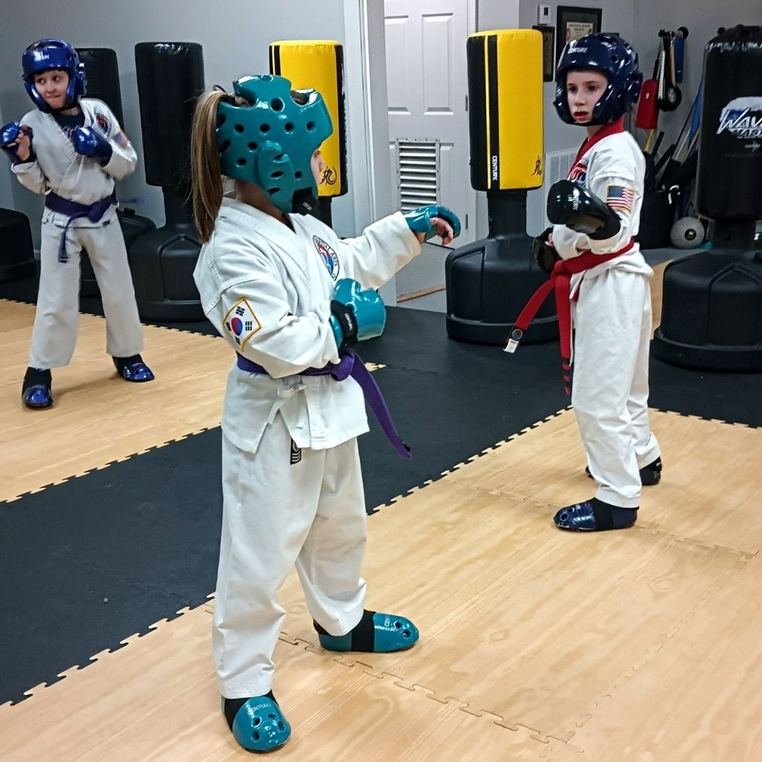 Two young children in blue and black martial arts uniforms grappling on a gym floor, one smiling.