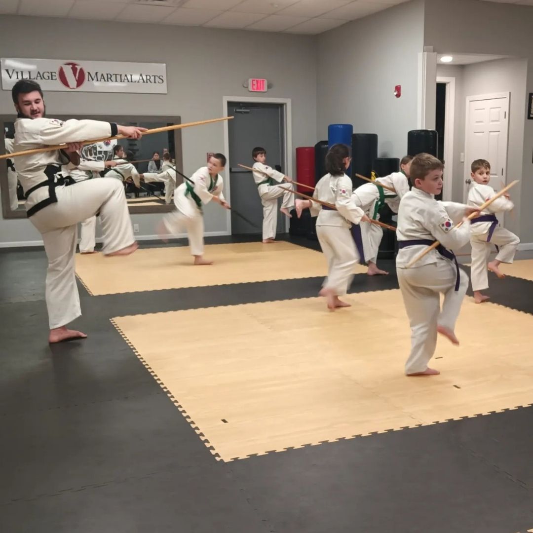 Two people grappling on a mat, one in a black gi, the other in a rash guard, legs entangled.