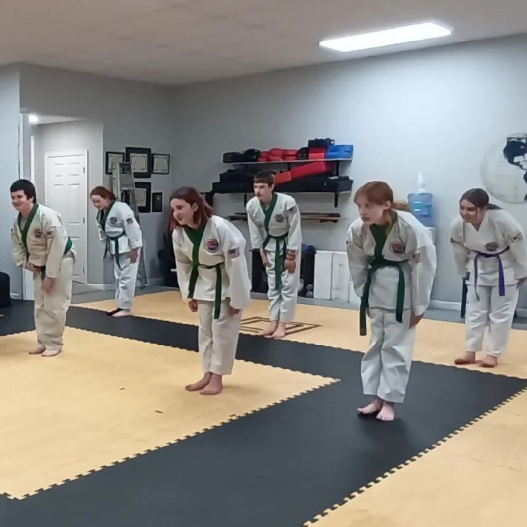 Five people in jiu-jitsu gear pose together in a gym.  Smiling,  some have arms around each other. Machado logo visible.
