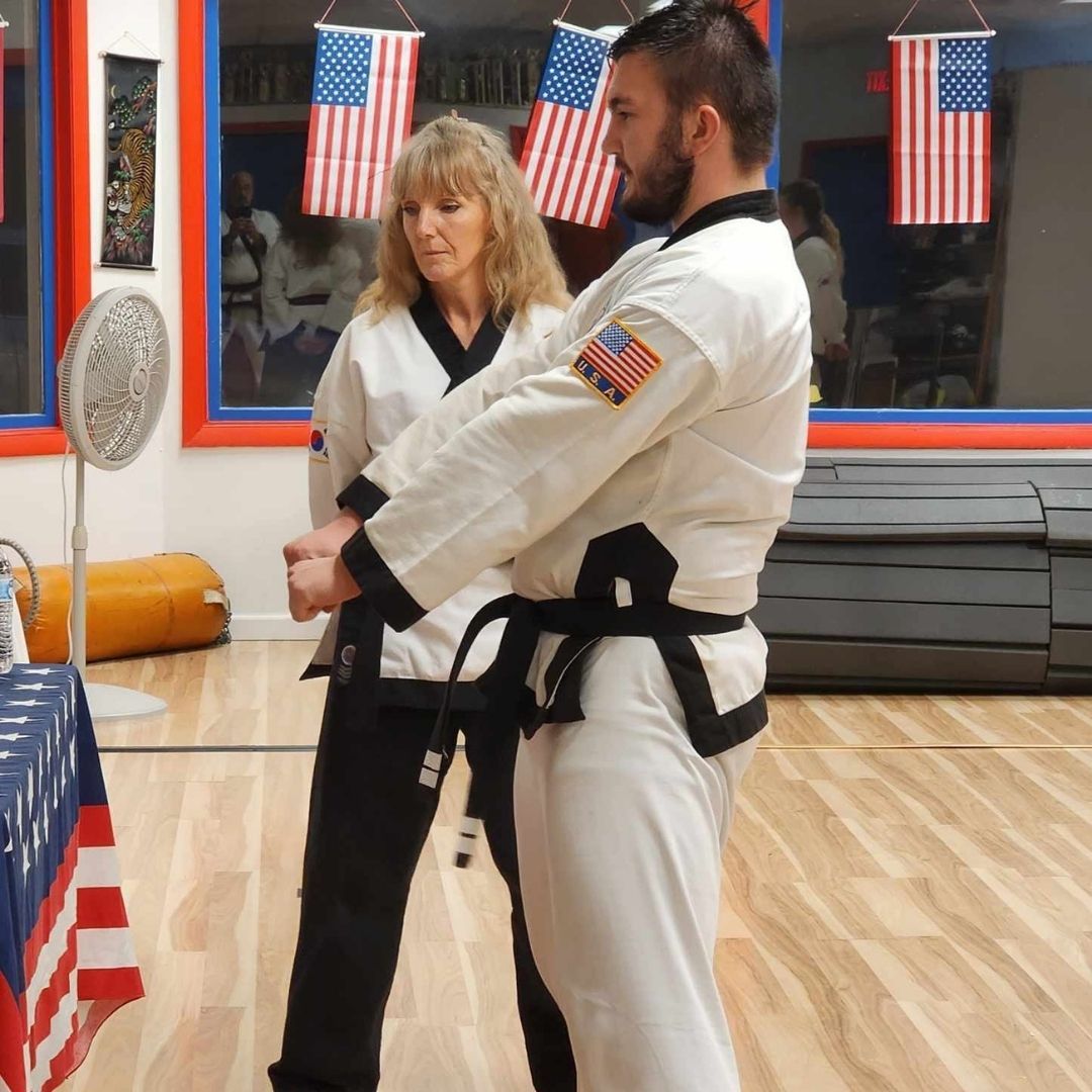Group of children in martial arts attire posing, some with arms around each other, in a gym.