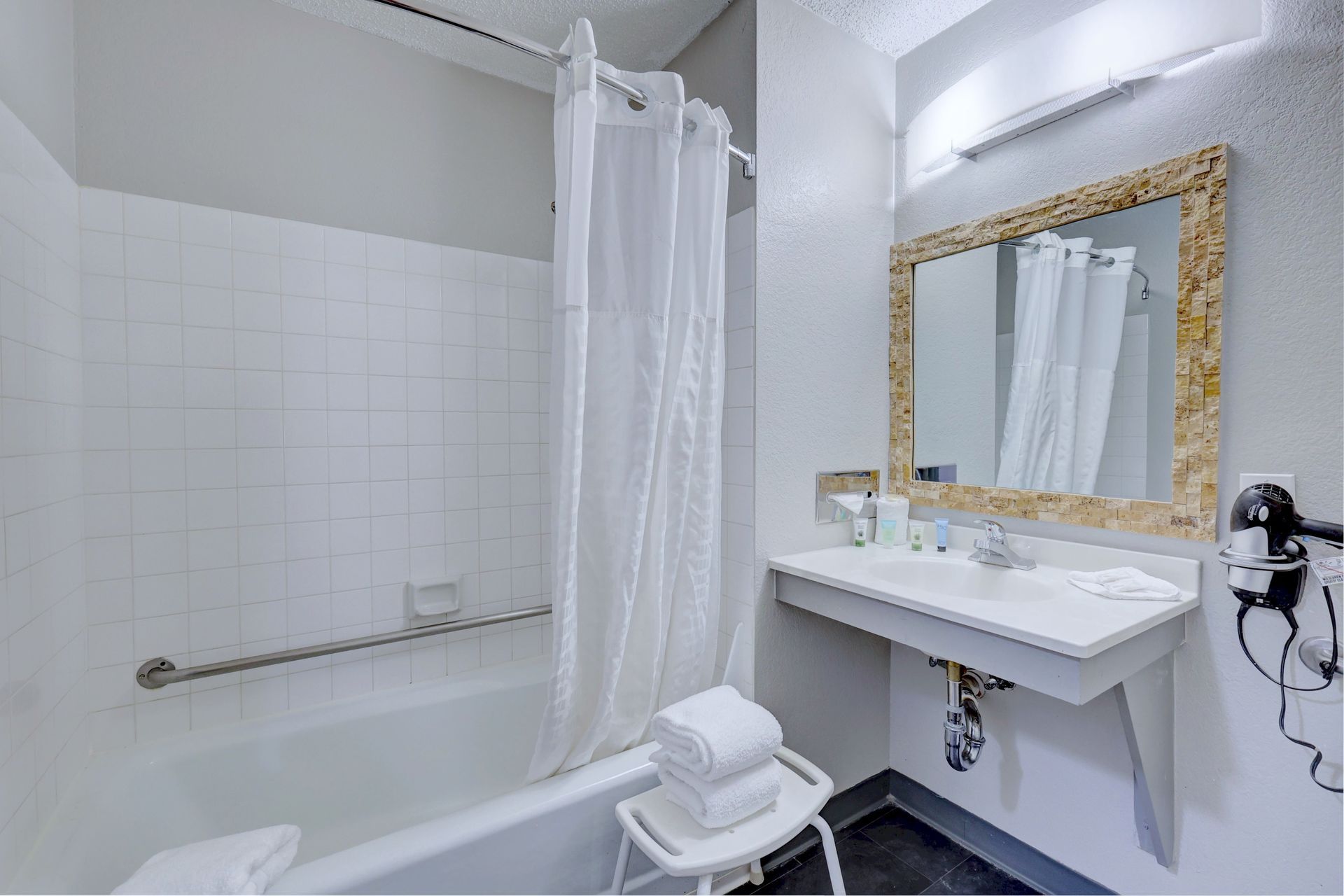A bathroom with a tub , sink , mirror and hair dryer.