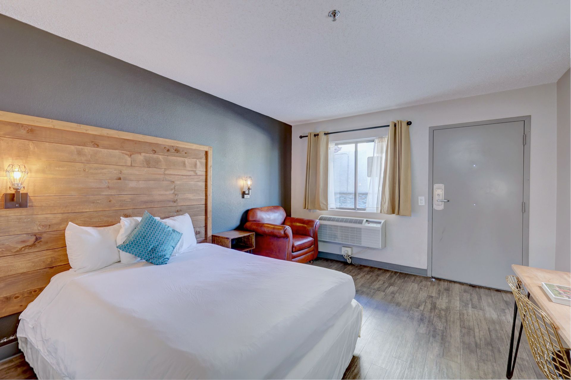 A hotel room with a king size bed , chair , desk and window.