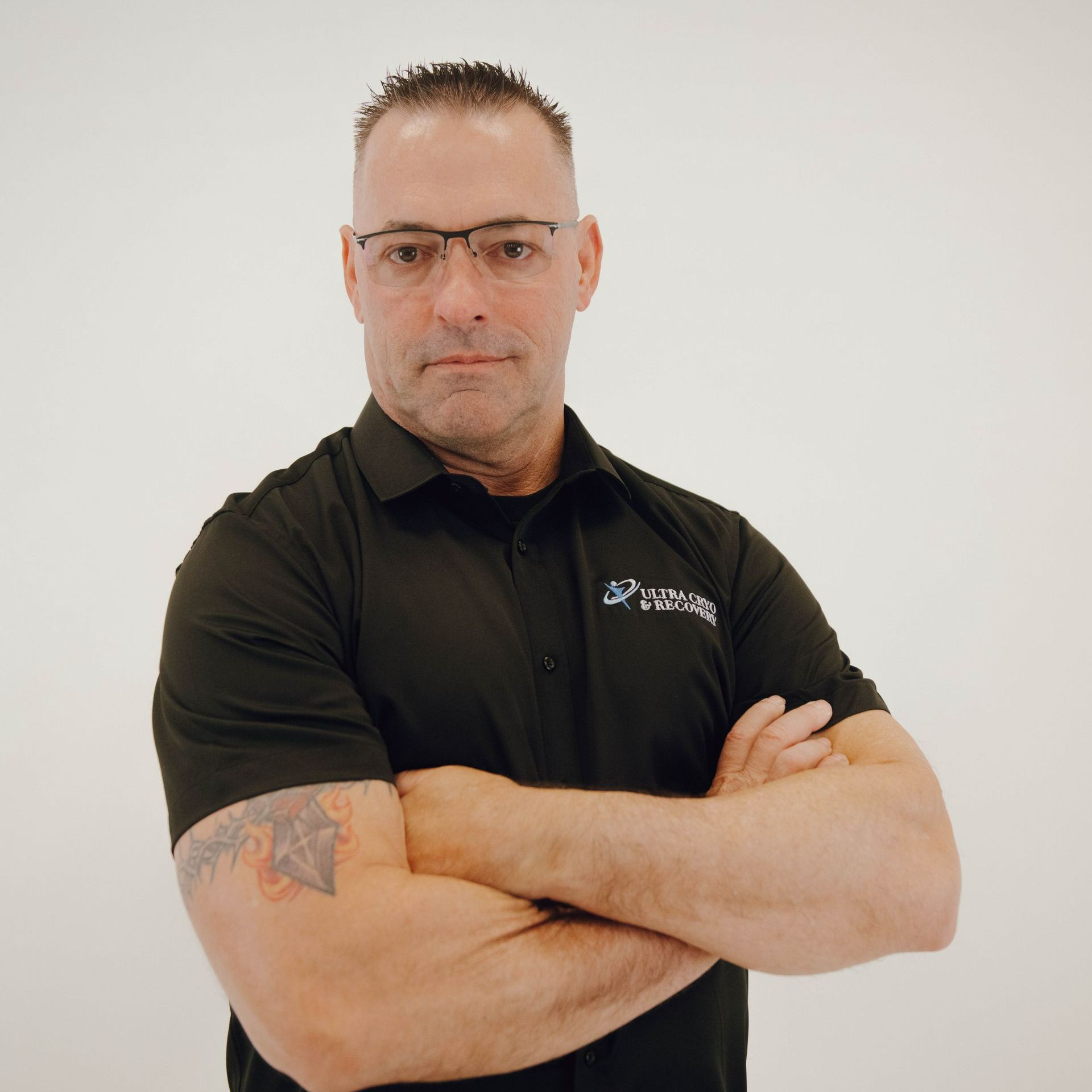 A man wearing glasses and a black shirt has his arms crossed