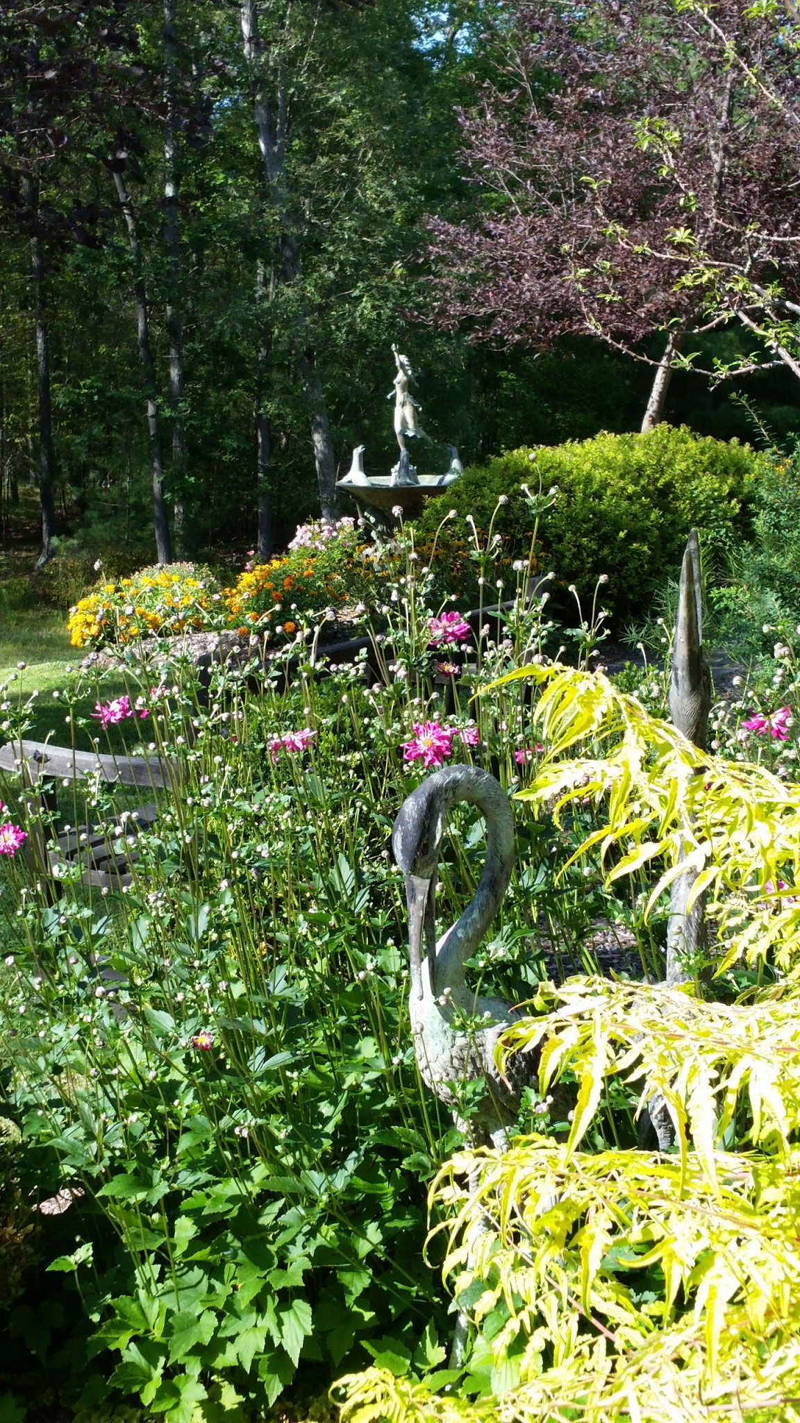 A swan statue is surrounded by flowers and trees in a garden.