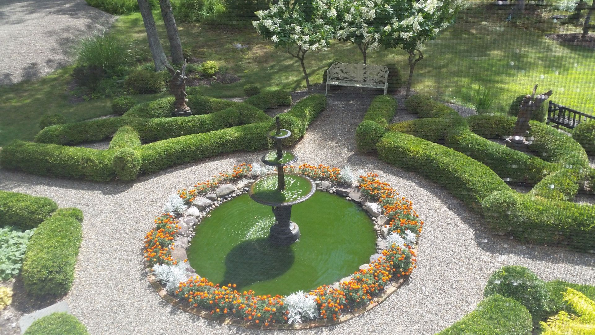 An aerial view of a garden with a fountain in the middle surrounded by flowers and bushes.