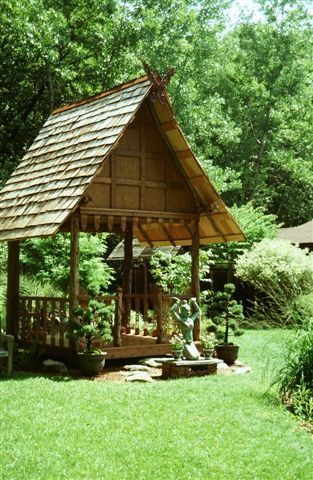 A small wooden gazebo in the middle of a lush green field