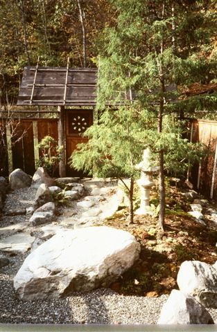 A garden with rocks and trees and a house in the background