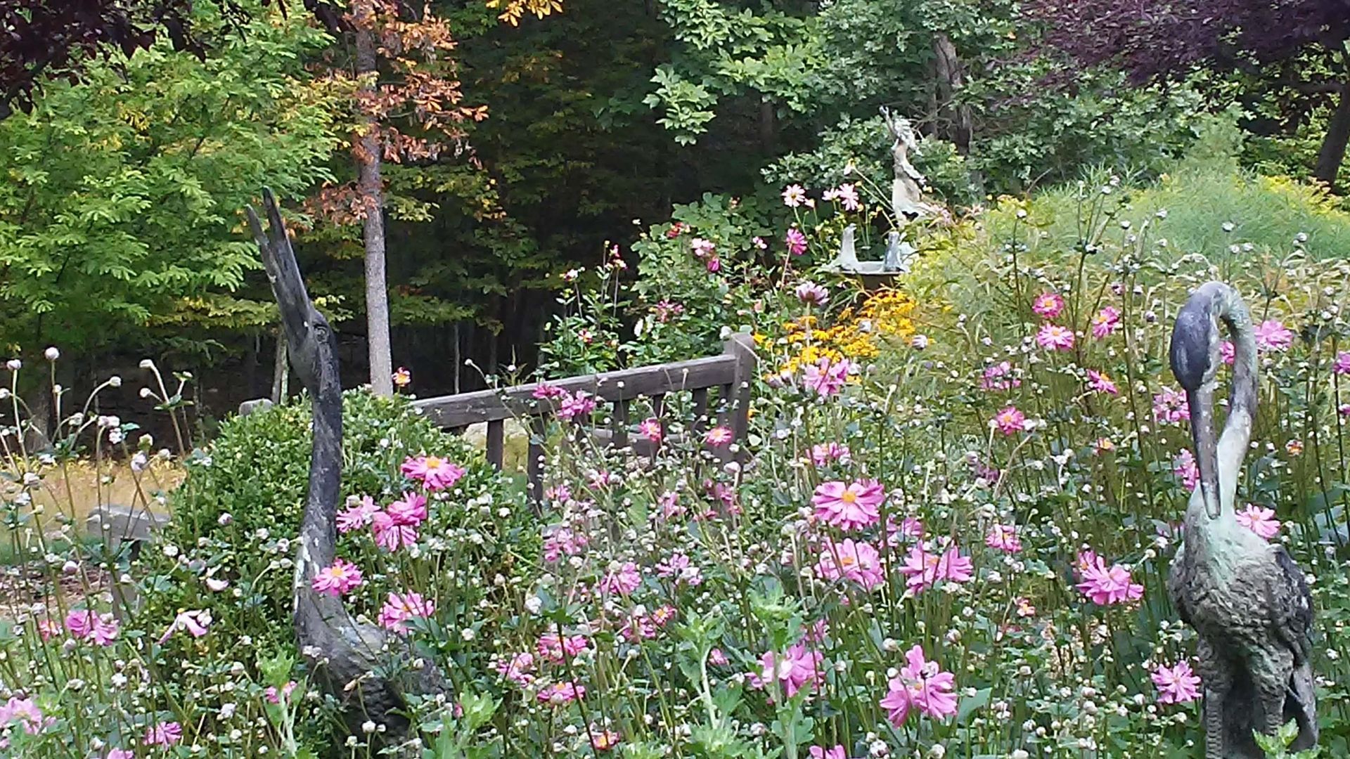 Two statues of birds are standing in a field of pink flowers.