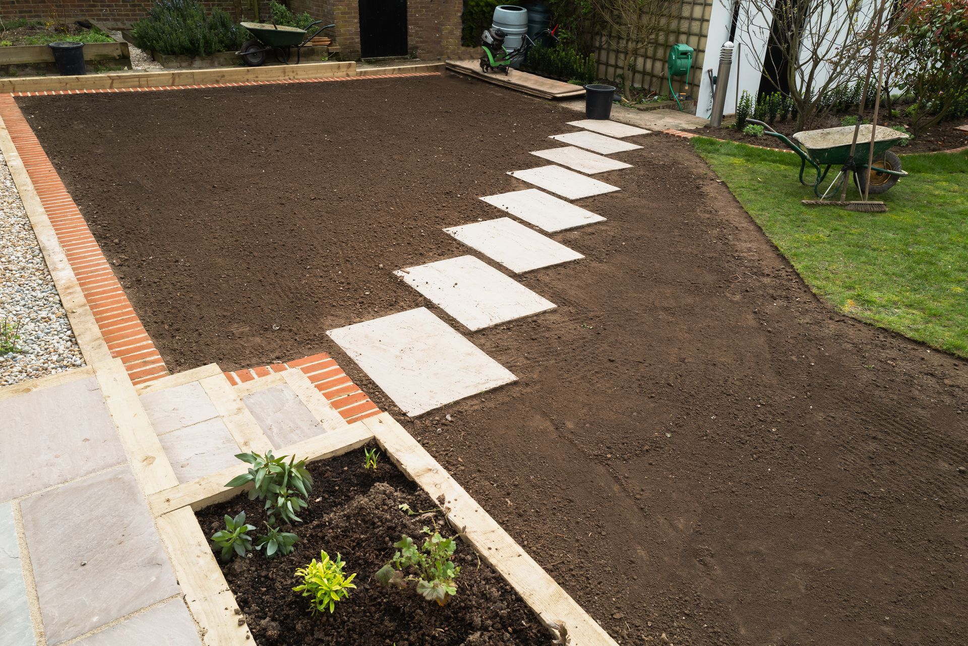 A garden with a walkway leading to a lawn and a wheelbarrow.
