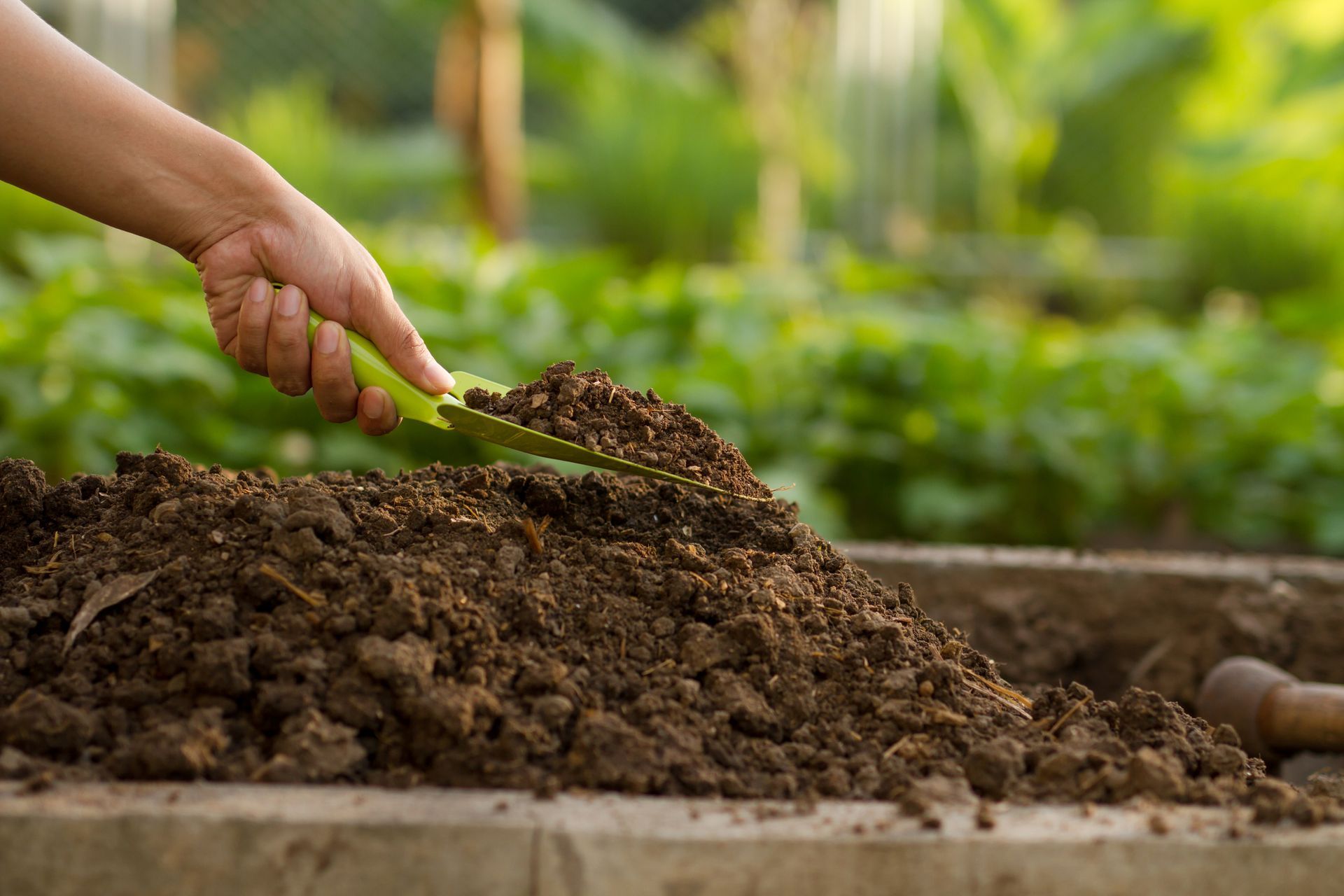 A person is shoveling dirt into a container with a trowel.