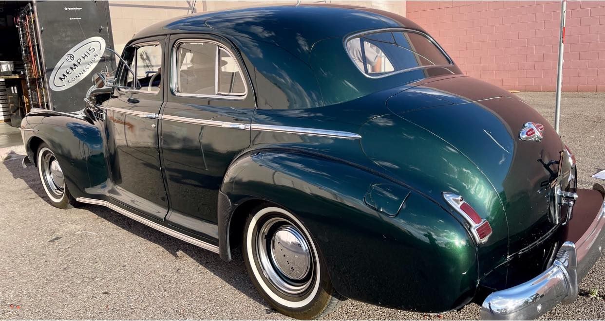 Green vintage car parked outside with its hood open.
