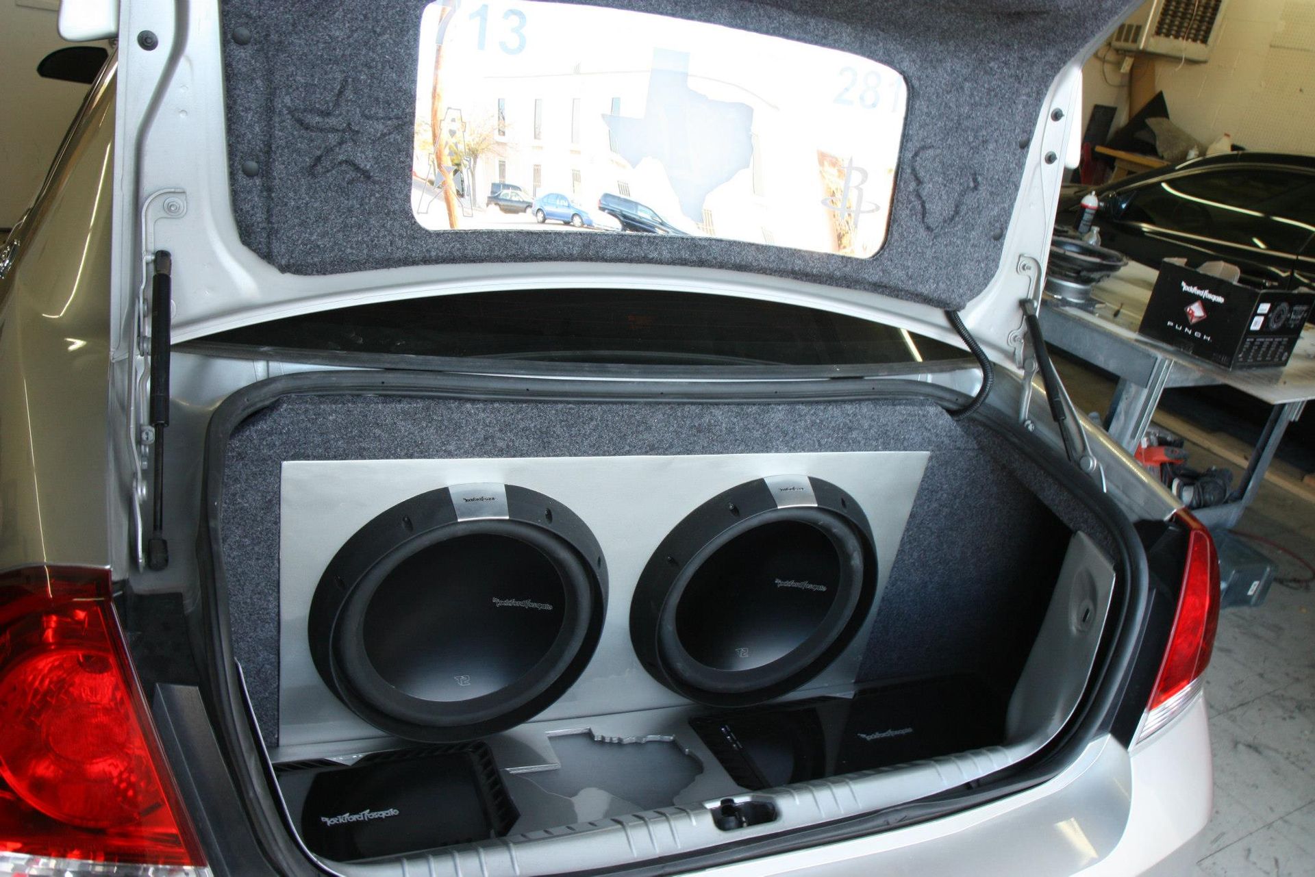 Silver car trunk with custom subwoofer enclosure containing two speakers.