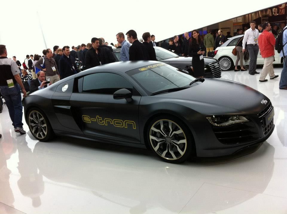 Grey Audi R8 e-tron electric car on display at an auto show, surrounded by people.