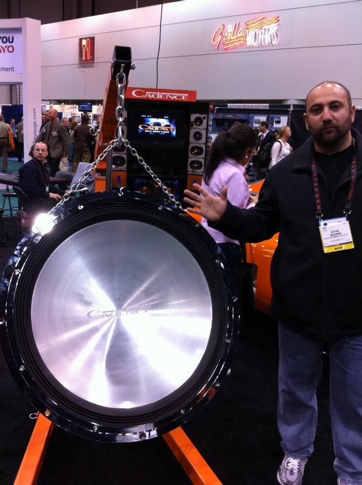 Man standing next to a massive car subwoofer on display at a convention.