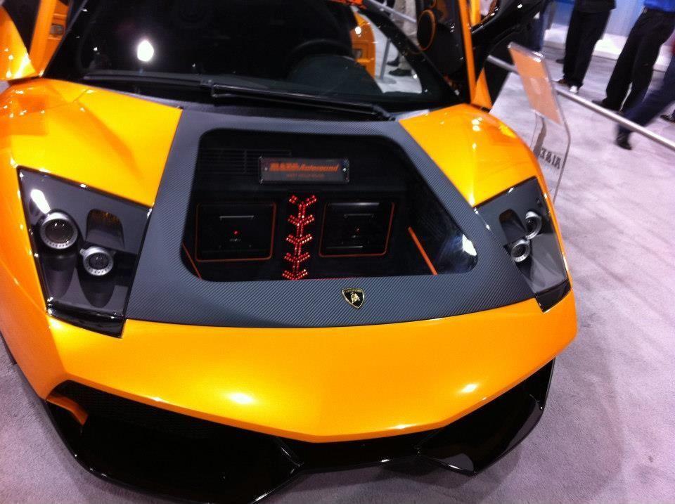 Yellow Lamborghini with doors open, showcasing a custom audio setup in the hood.