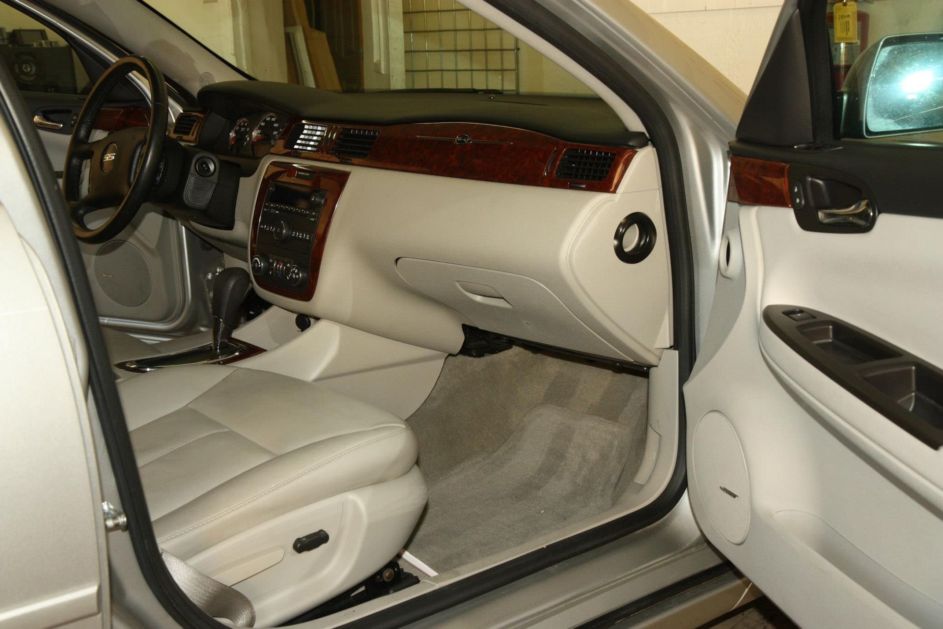 Silver car interior: beige seats, wood trim, dashboard, open door, driver's seat visible.