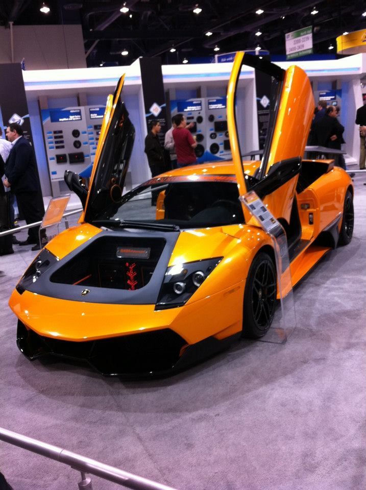 Orange Lamborghini with doors open, on display at an event.