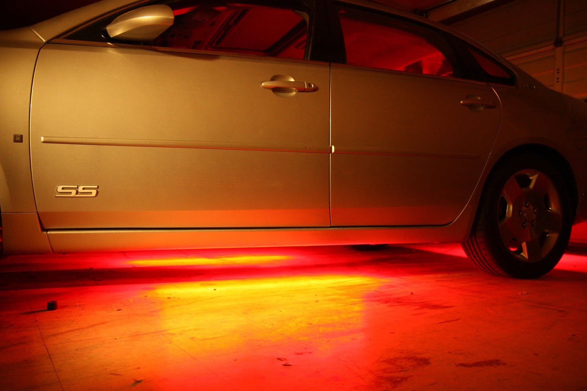 Silver car with red underglow illuminating the concrete floor.