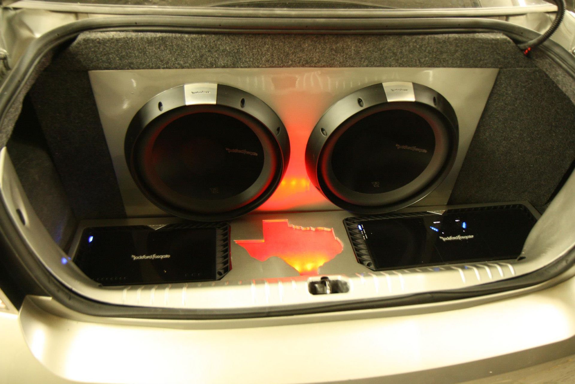Car trunk with two large subwoofers, amplifiers, and a glowing Texas outline.