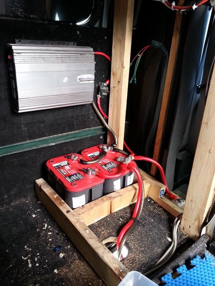 Three red car batteries wired to an inverter. The batteries are in a wooden frame.