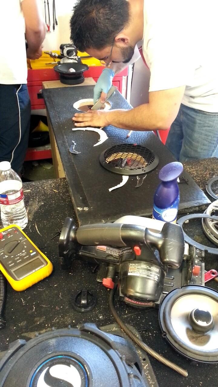 Man working on a speaker, cutting a design on a black surface with other parts and tools visible.