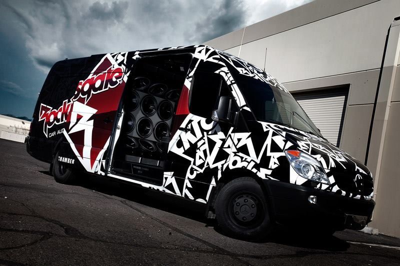 Van covered in abstract black and white shapes and Rock'n'Roll logo; door open revealing speakers.