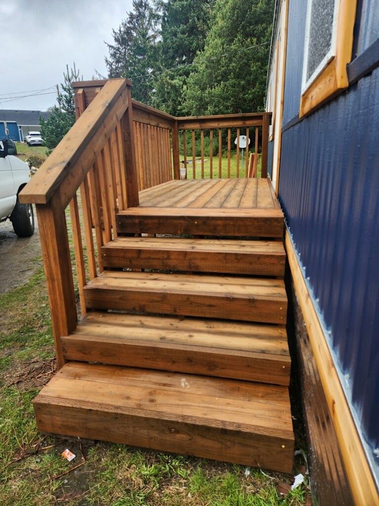 A wooden deck with stairs leading up to it is next to a blue house.