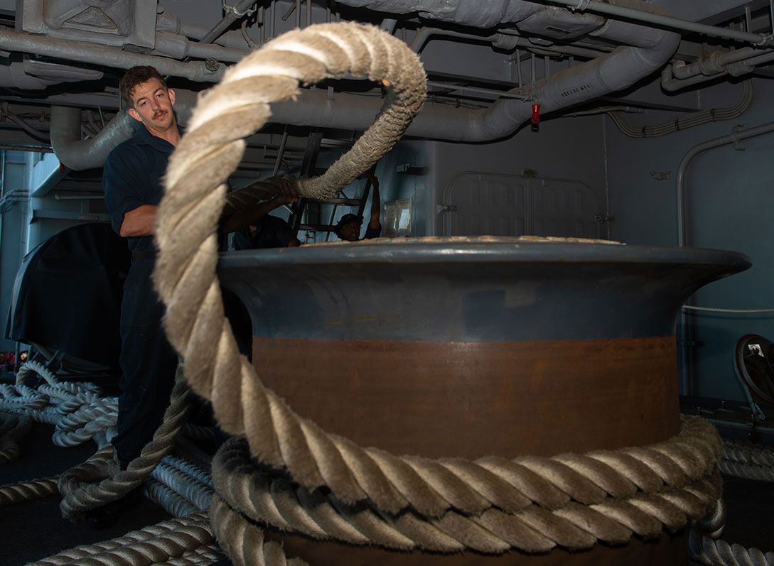 A man is standing next to a large rope on a boat.