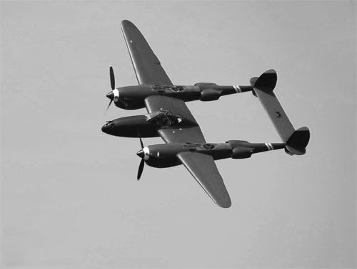A black and white photo of a propeller plane flying in the sky