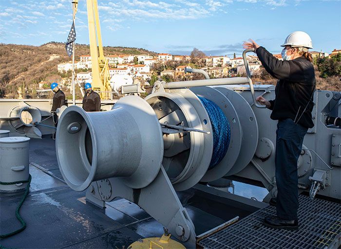 A man in a hard hat is standing next to a large machine on a boat.