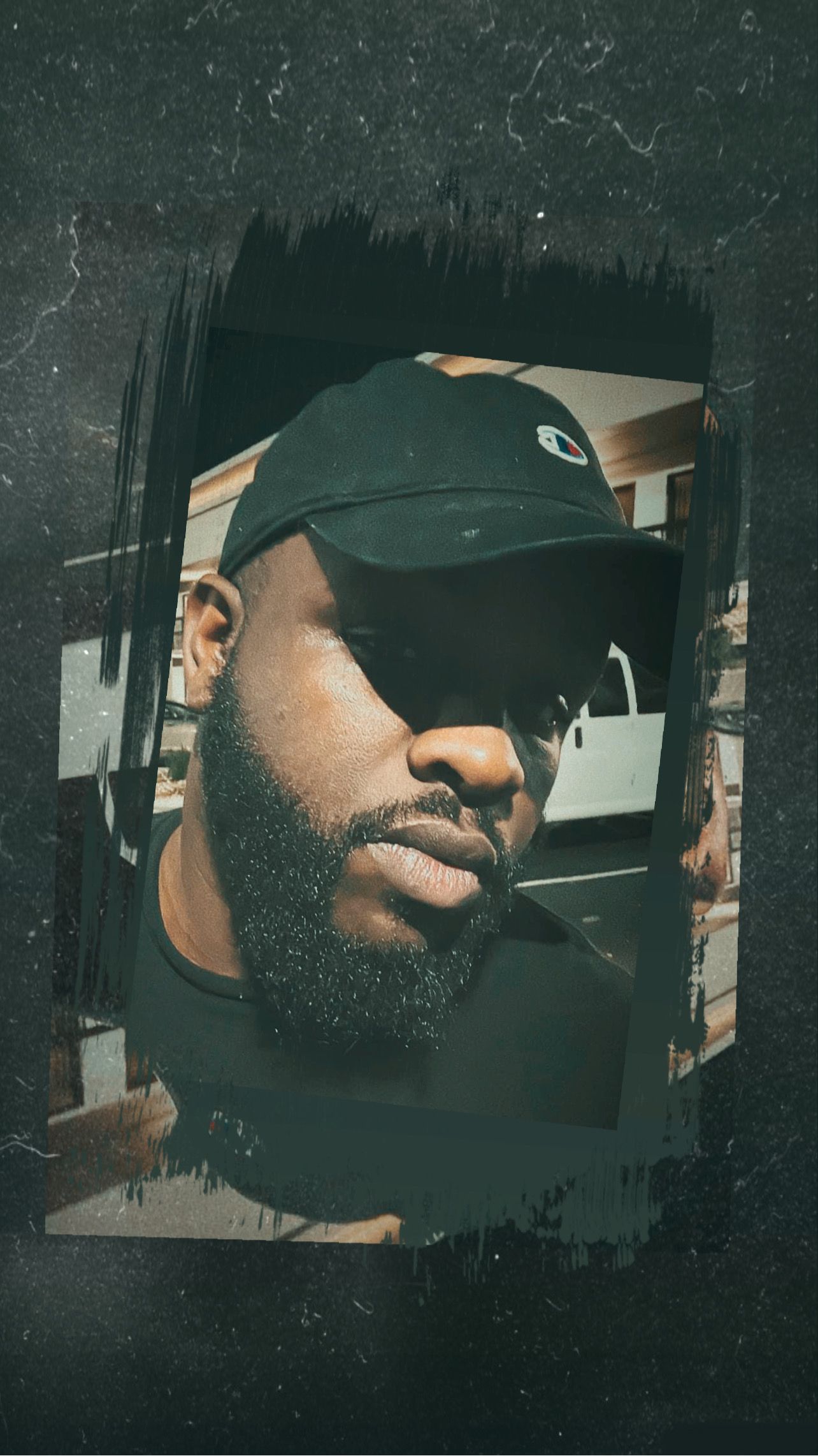 Man with a beard and cap, looking towards the camera. Black and white aesthetic with a grunge frame.