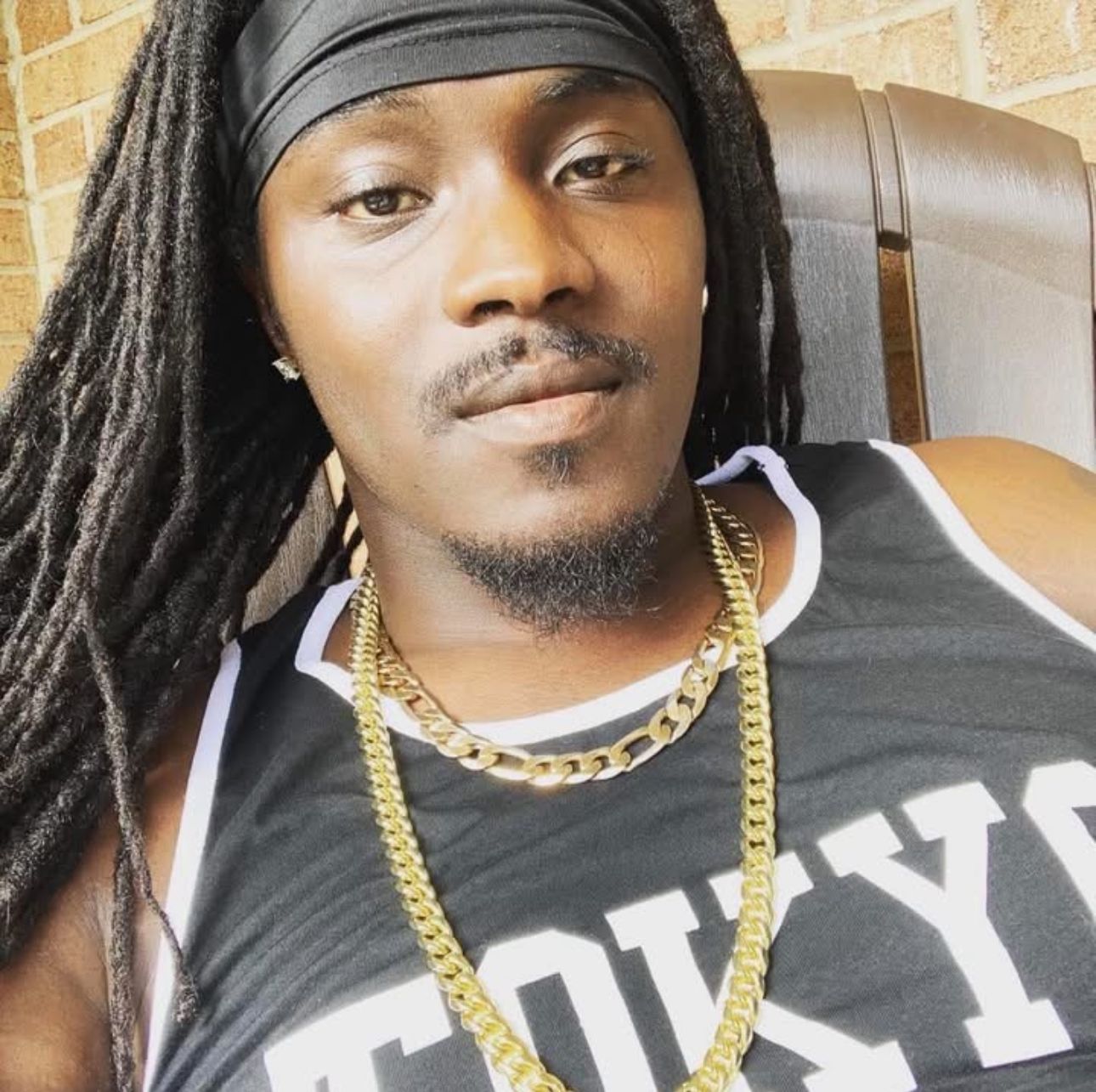 Man with dreadlocks, wearing a gold chain and a black tank top.