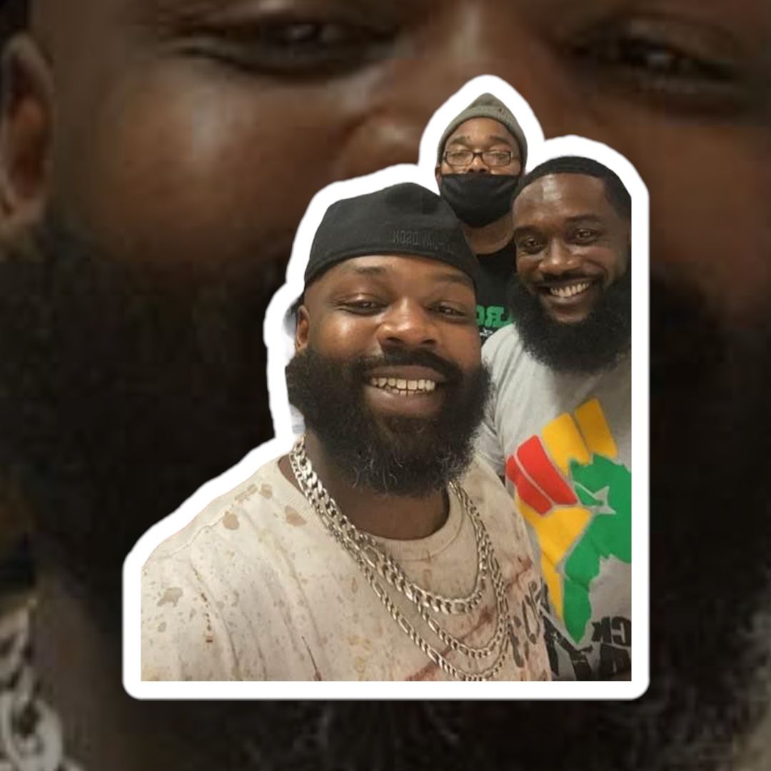 Three Black men smile, one with a gold tooth, posing for a selfie, indoors.