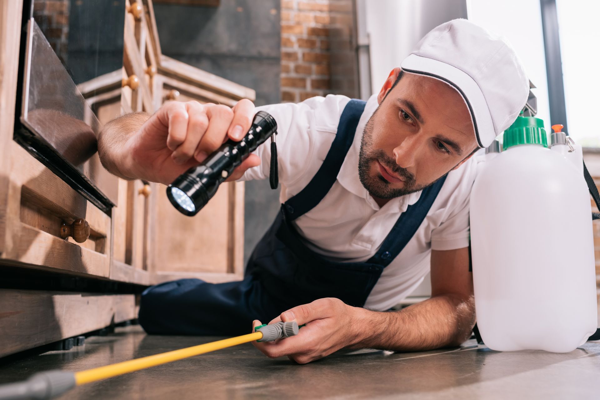 Worker in white cap and apron cleaning an oven with a brush and spray bottle in a kitchen