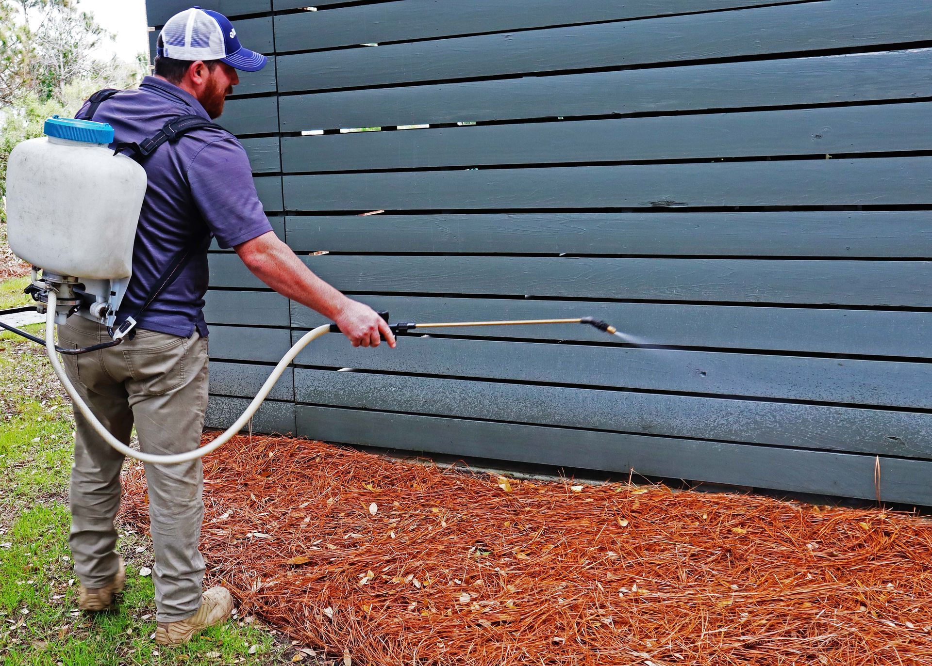 Person spraying a blue wall outdoors with a backpack sprayer