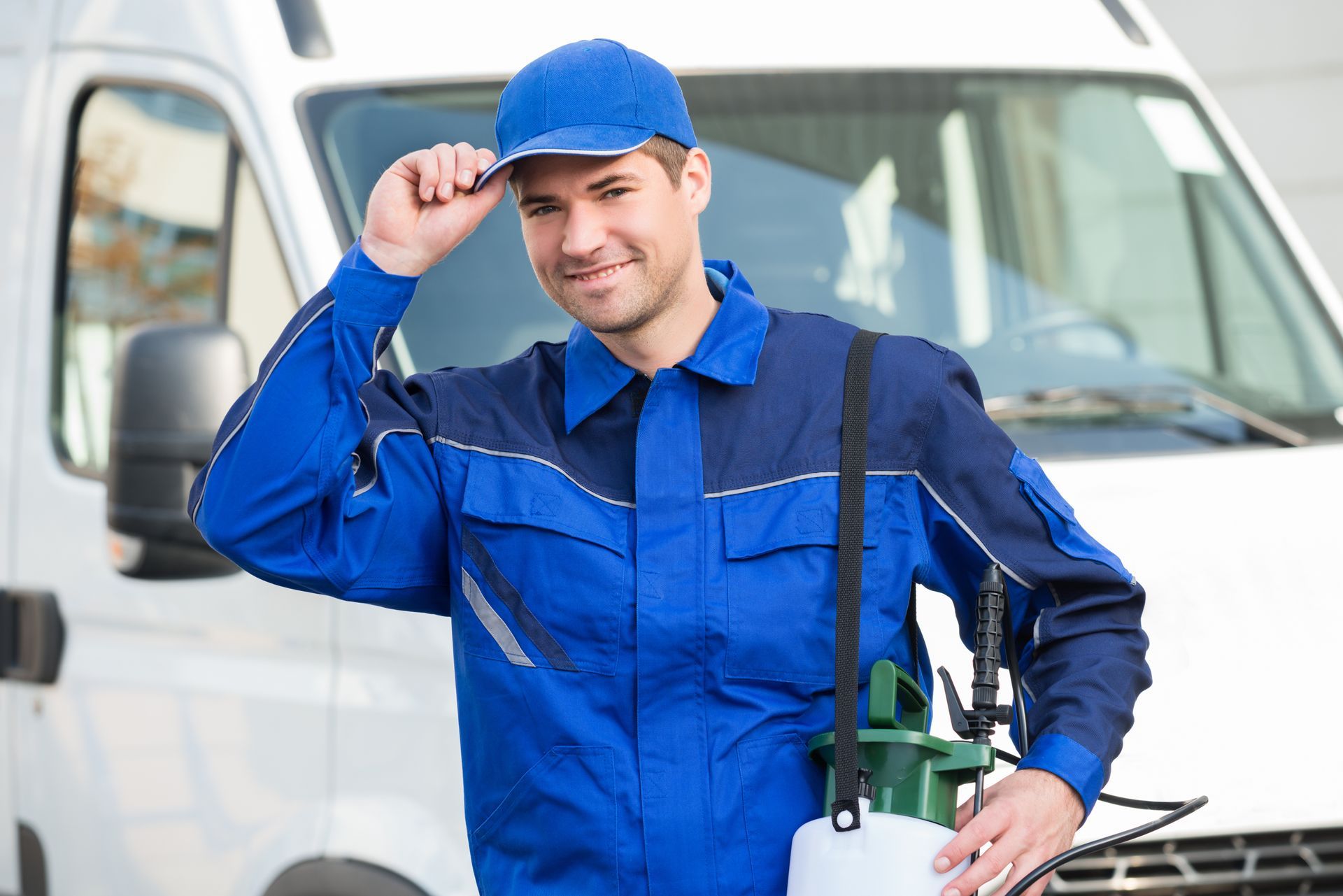 Blue-uniformed worker tipping cap beside a white van, holding a fuel nozzle outdoors
