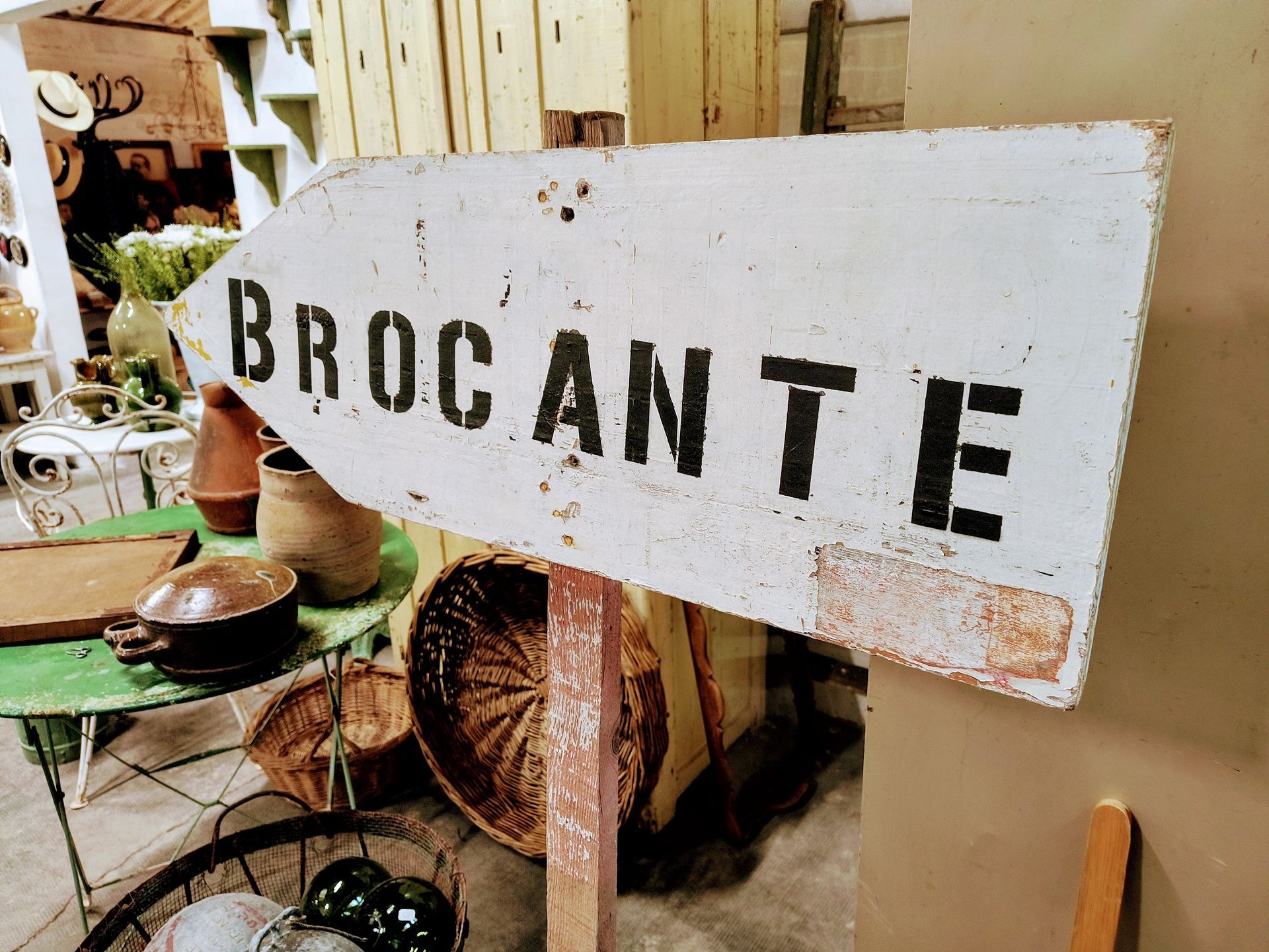 Sign post that says brocante surrounded by baskets at a market