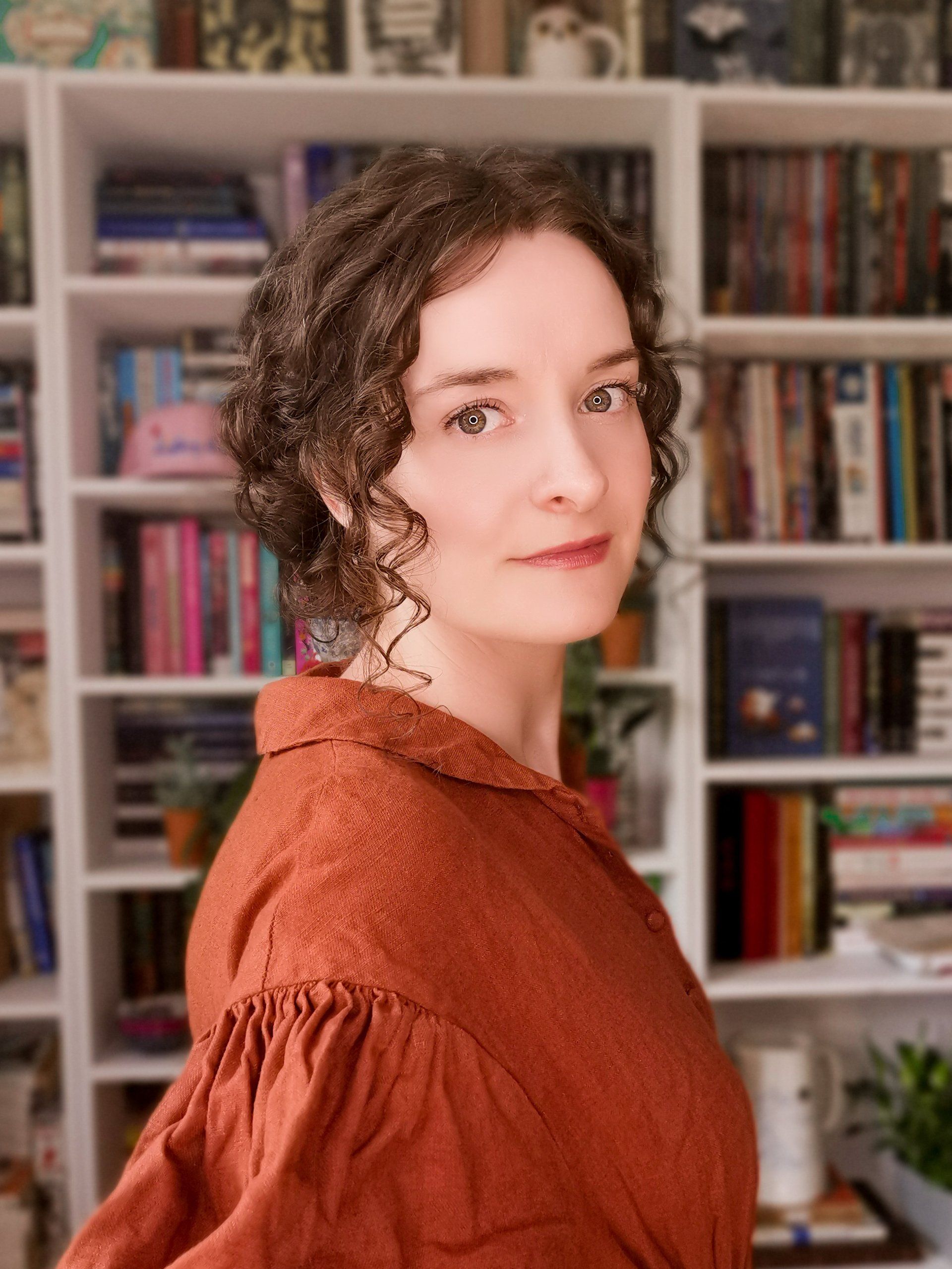 A woman with curly hair is standing in front of a bookshelf.