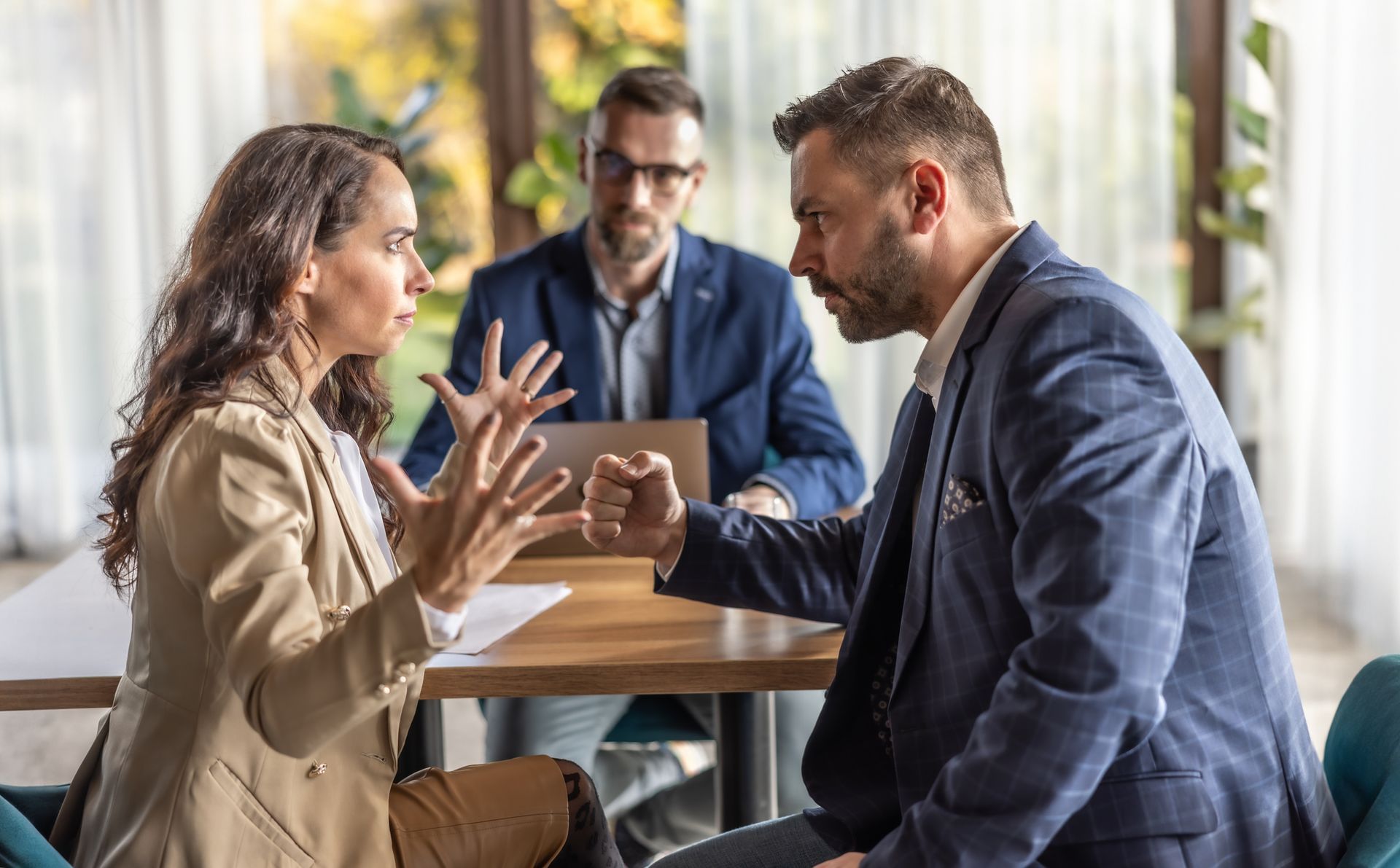Woman and man in business attire arguing; a man in the background observes.