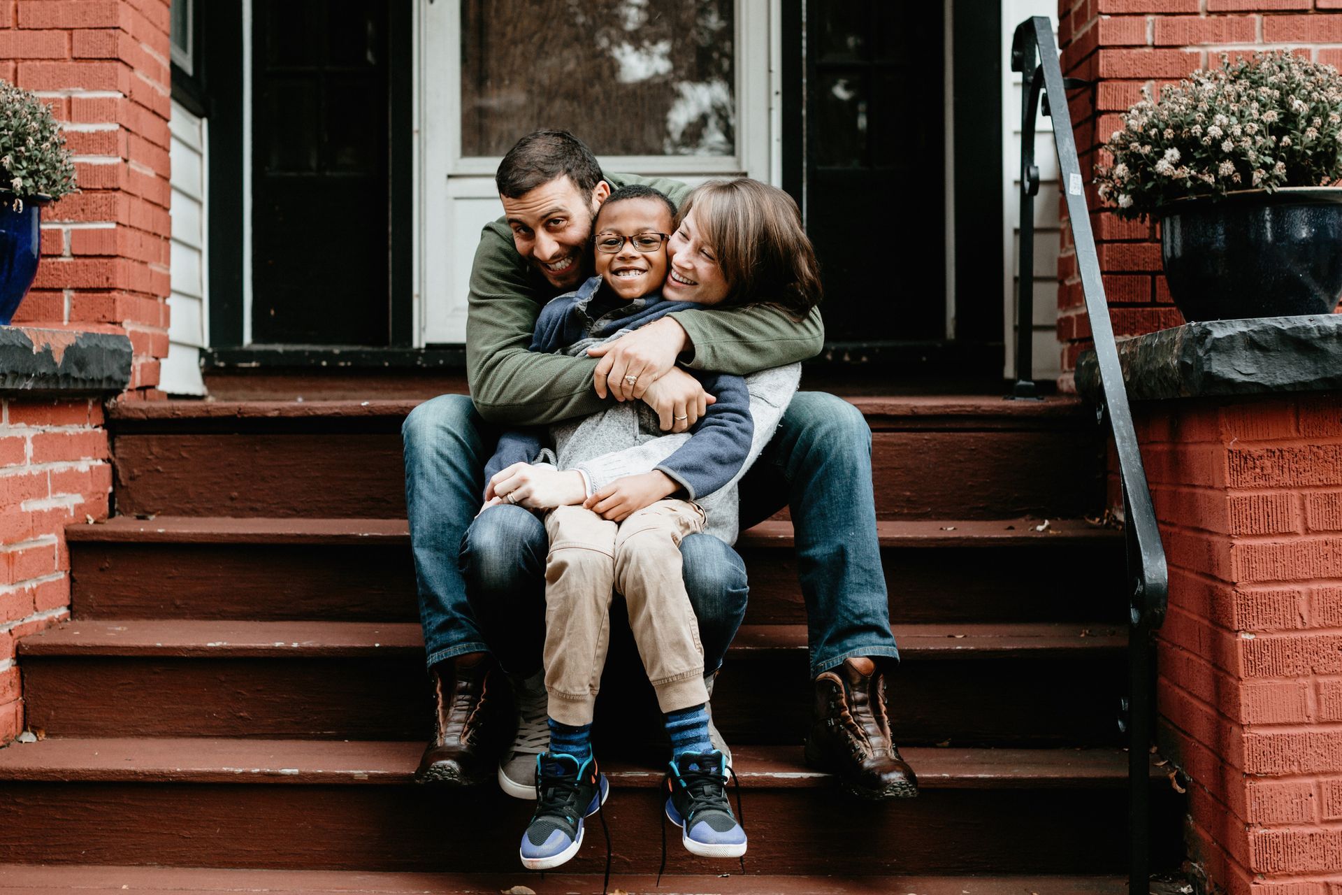 Family of three embracing on brick steps; father hugs son, mother wraps arms around them.